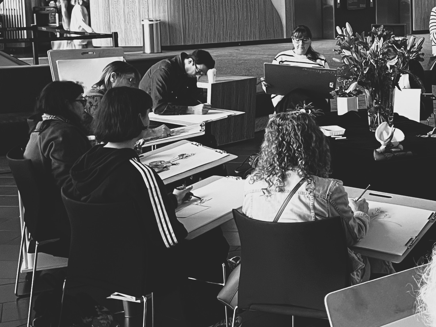 group of people sitting down drawing a still life display