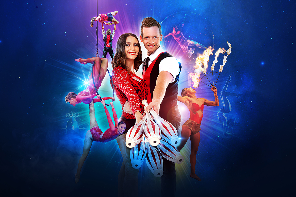 A woman in a red dress stands behind a man in a red vest, with Cirque Nouvelle performers (acrobats) in the background