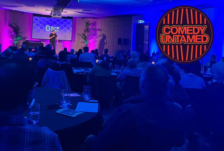 A man stands on stage doing a comedy stand up while people are dining 