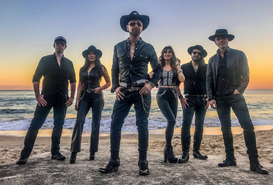 Six people in dark clothing stand against a bright sunset - members of Pseudo Echo