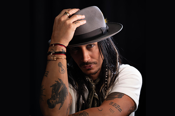 A man in a white t-shirt holds a hat on his head