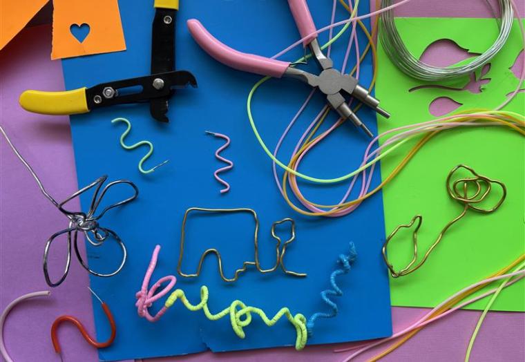 Flatlay of wire and pliers with purple blue and green coloured paper in the background