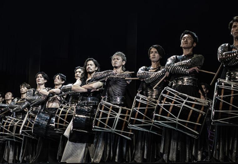 A line of drummers set against a dark background - Drum Tao