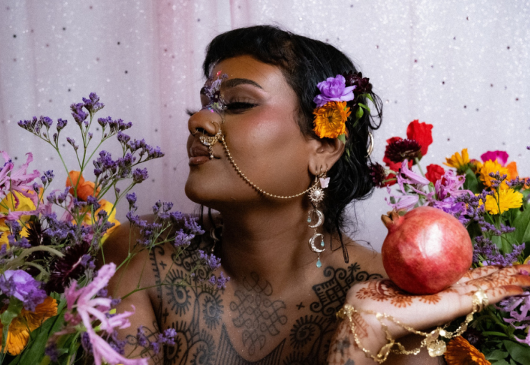 A woman with a flower in her hair is surrounded by other flowers