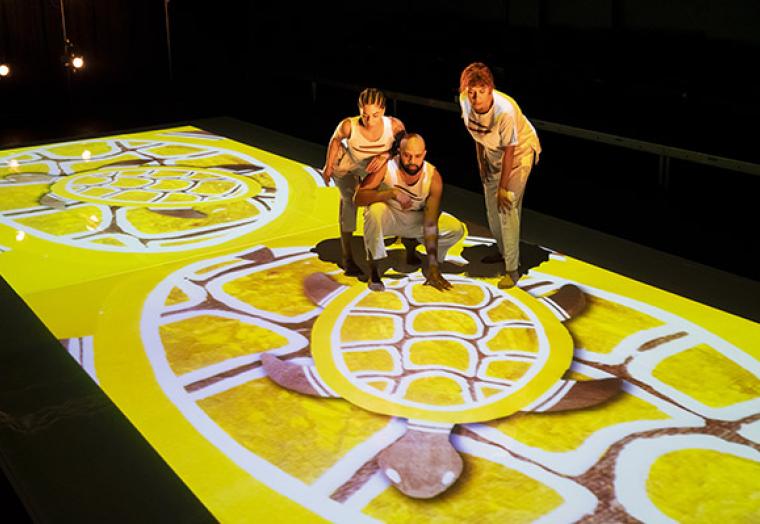 Three indigenous performers stand on an art digital projection