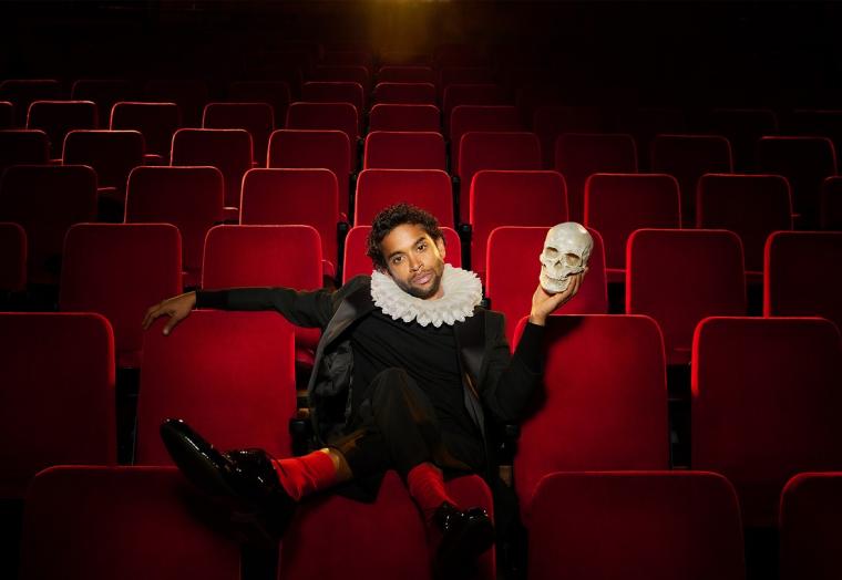 A man sits in a theatre holding a skull. 