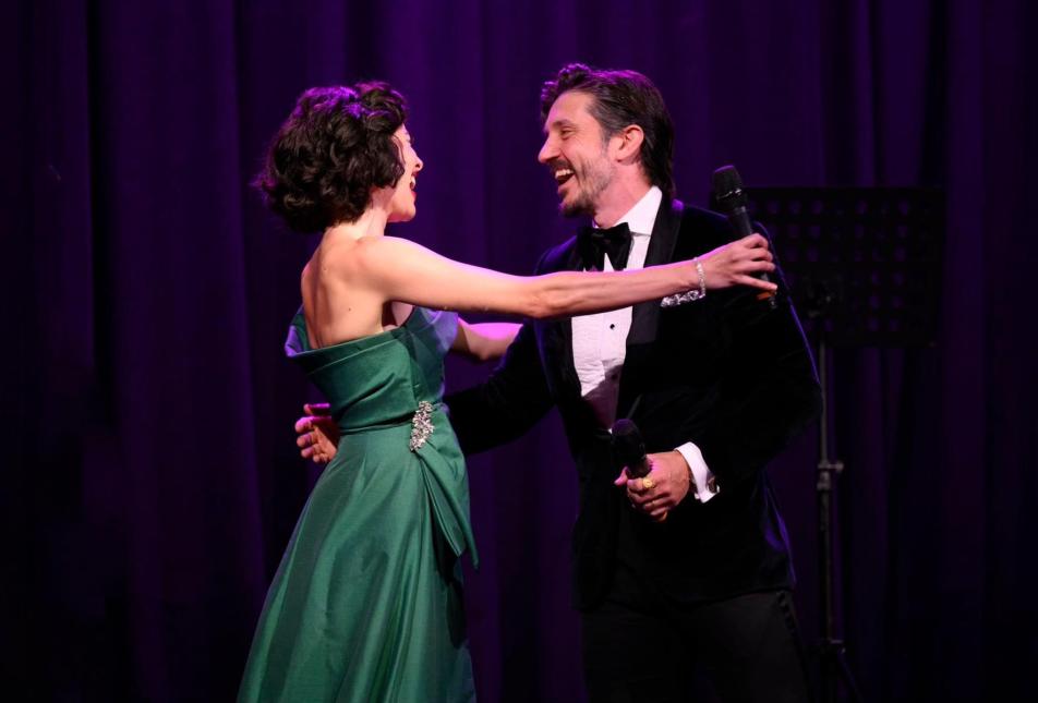 A woman in a green dress hugs a man in a black suit