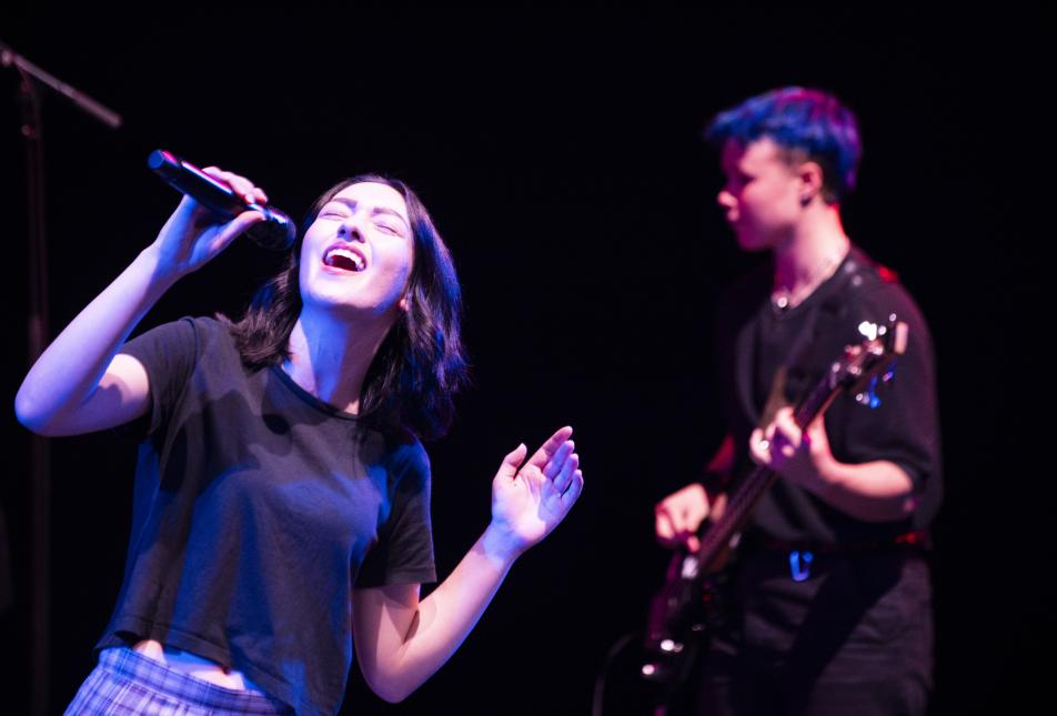 two student band performers, one with a microphone the other playing the electric guitar