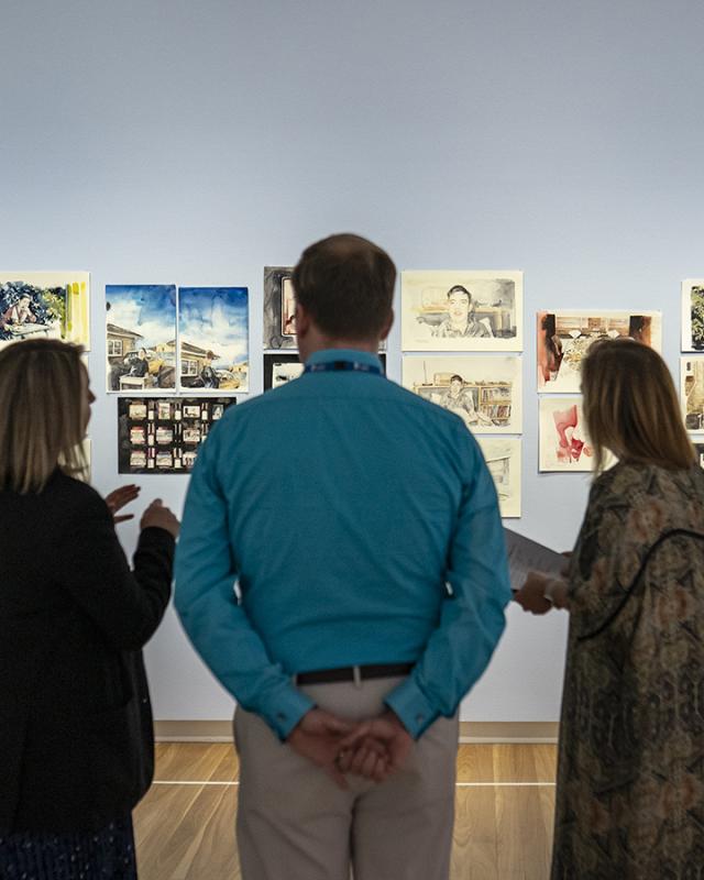 Three people look at paintings on gallery wall