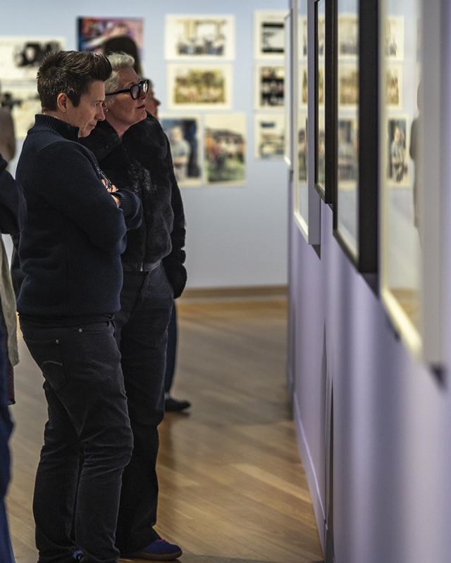 Several people stand in an art gallery looking at paintings on the wall