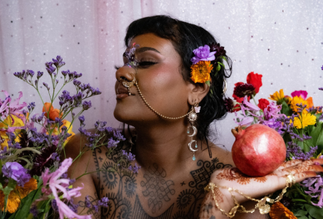 A woman with a flower in her hair is surrounded by other flowers