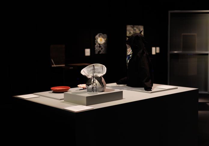 installation view of a display featuring a ceramic vase, a black hoodie and rope bowls