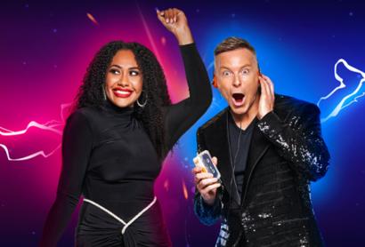 A woman in a black dress dances with her hand up in the air while a man in a suit has a surprised look on his face. 