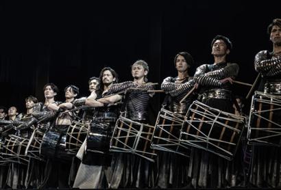 A line of drummers set against a dark background - Drum Tao
