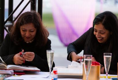 Two people sitting next to each other cutting out images, smiling and drinking wine