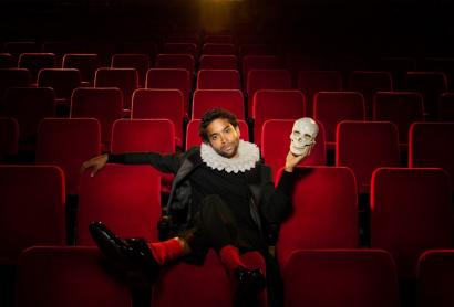 A man sits in a theatre holding a skull. 